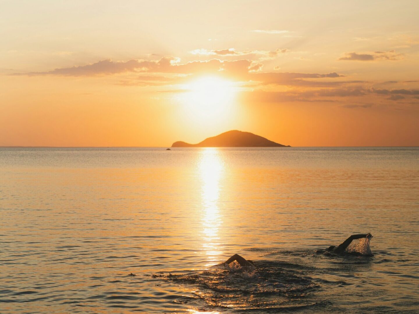 Two people swimming in ocean at sunset with island in background