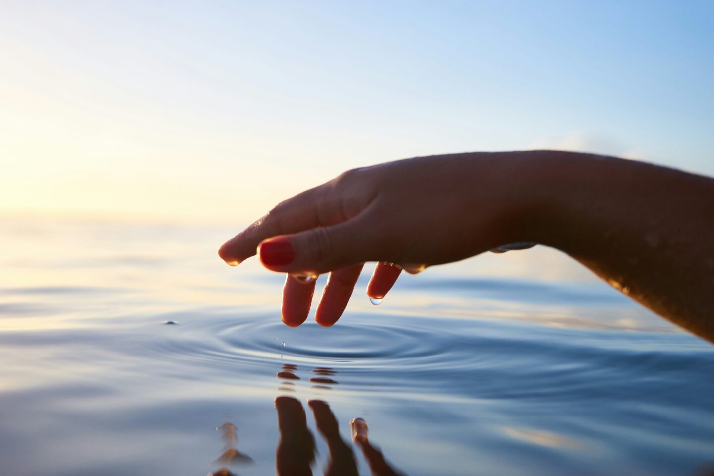 Hand touching ocean water with finder tips as sunsets
