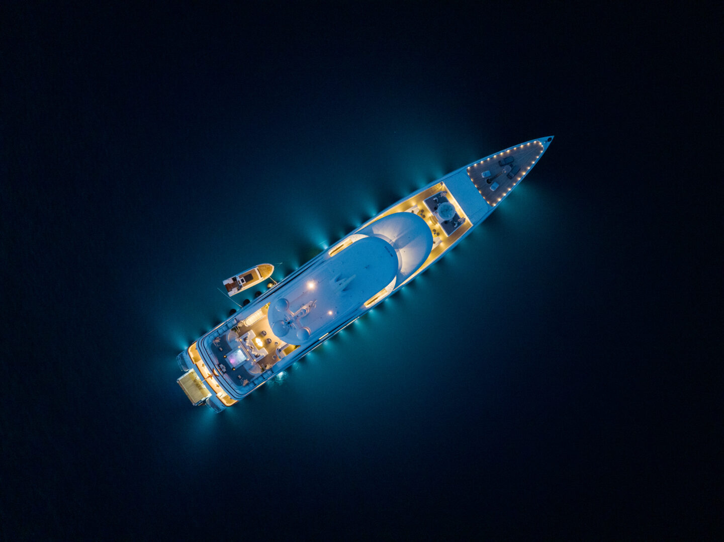 M/Y Soundwave for charter at anchor at night, illuminated in an aerial view. Credit: Roccabella / Huber.