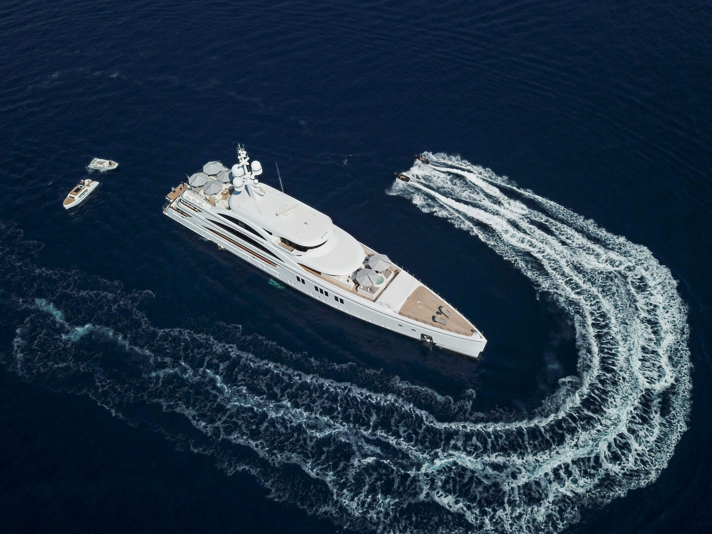 M/Y Soundwave for charter at anchor in an aerial view with a smaller boat circling the superyacht. Credit: Roccabella / Malcorps.